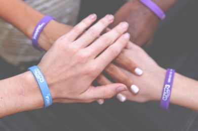 4 people wearing CREATE wristbands put their hands together for a photo